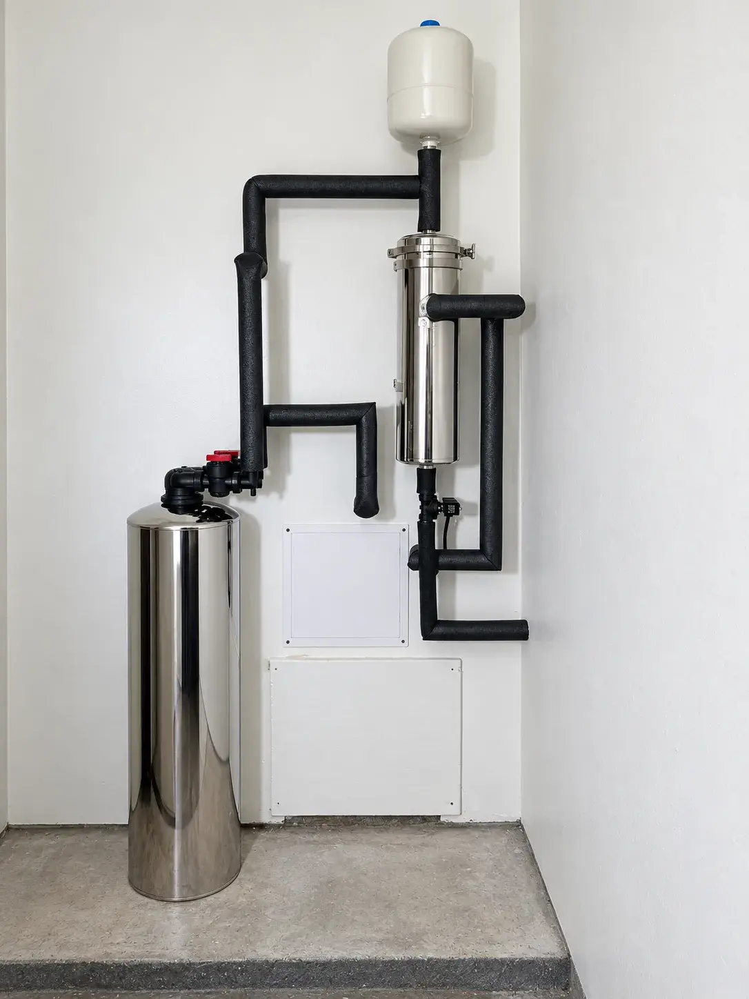 Whole-house water filtration system with stainless tanks and insulated pipes installed against a utility wall